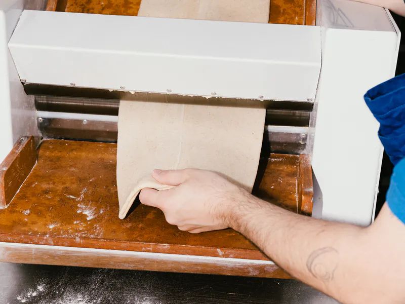 Bloque de masa laminada con manteca saliendo de la laminadora, en la cocina de honesto