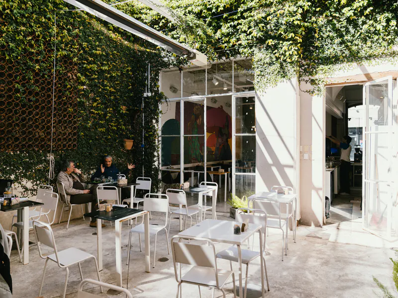 Patio de honesto con mesas blancas, plantas y clientes conversando