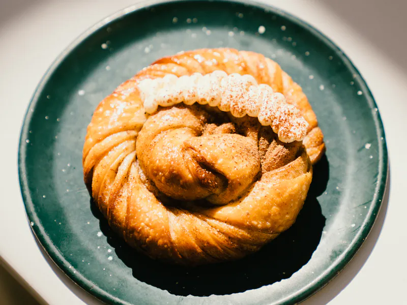 Roll de canela de manteca con azúcar en plato, laminados de honesto bakery