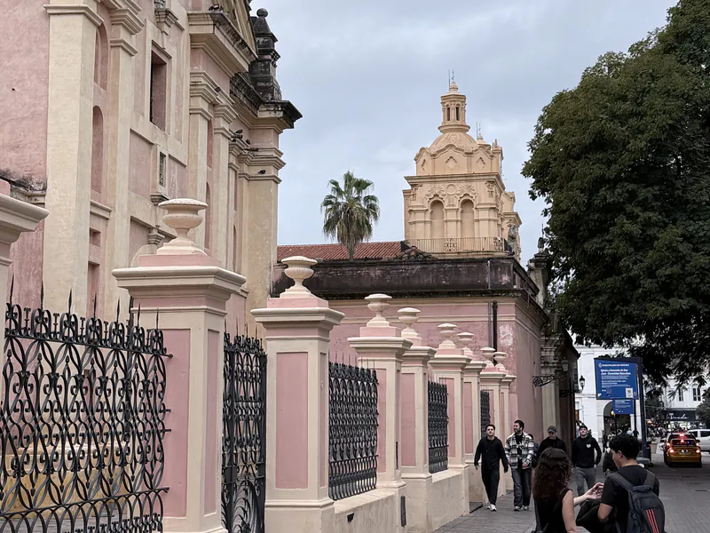 Fachada rosa de la Iglesia de Santa Teresa sobre la calle Independencia, con la cúpula de la Catedral de Córdoba al fondo y gente caminando por la vereda
